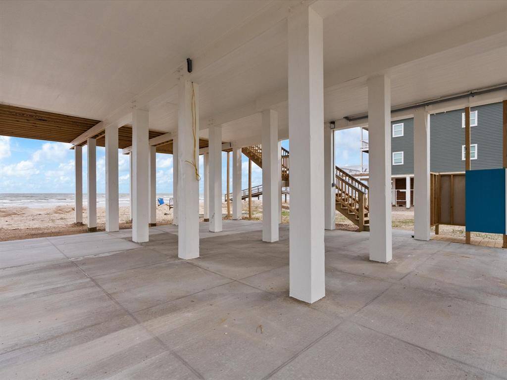This photo showcases an open, covered ground-level area of a beachfront property with sturdy support columns and a view of the ocean. Ideal for parking or outdoor gatherings, it offers easy beach access and coastal living charm.