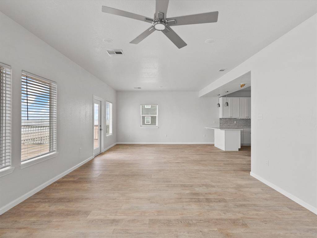 This spacious, open-concept living area features light wood flooring, large windows for natural light, a ceiling fan, and a modern kitchen with a breakfast bar. Perfect for entertaining and family gatherings.