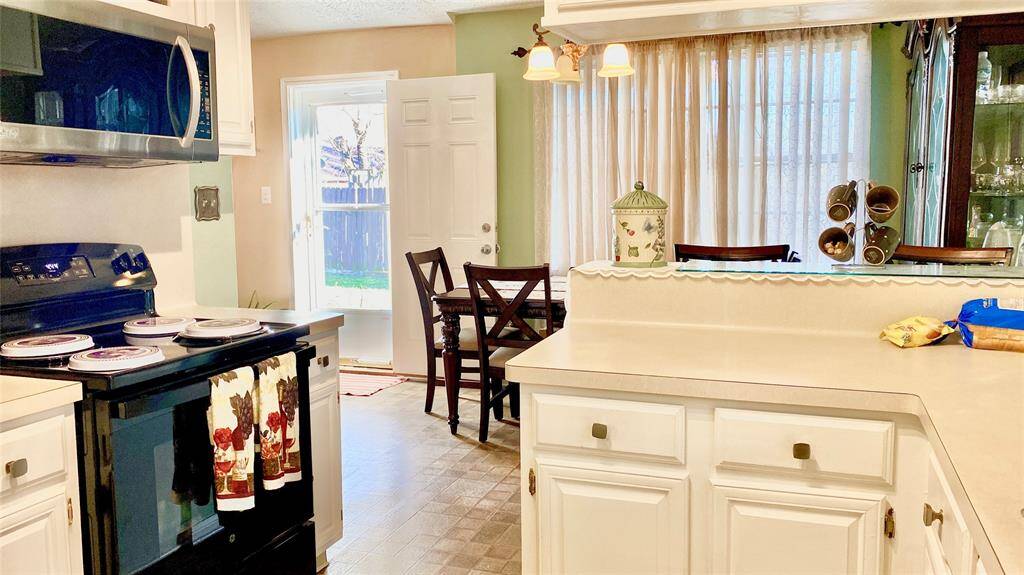 Cozy kitchen with white cabinetry and modern appliances. There's a breakfast bar overlooking a dining area with natural light from large windows and a door leading to the backyard. The space is inviting and functional, perfect for family meals.