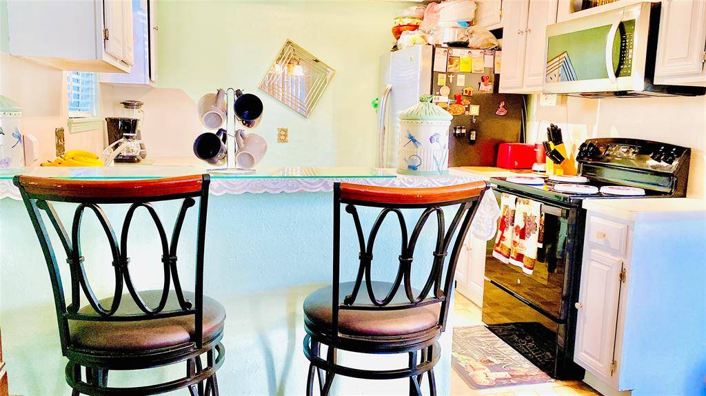 This cozy kitchen features a breakfast bar with two stylish chairs, a well-equipped cooking area with modern appliances, and ample storage with white cabinets. The space is bright and inviting, perfect for casual dining and meal preparation.