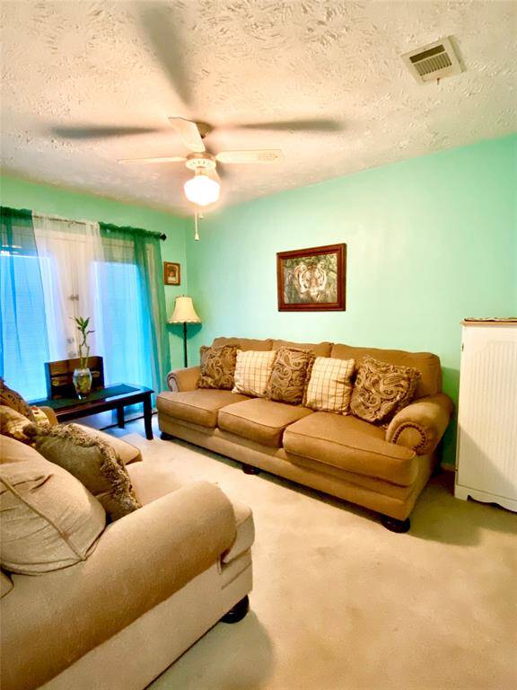 Cozy living room with soft, beige sofas and decorative pillows. Features a light turquoise wall, ceiling fan, and large window with sheer curtains for natural light. Ideal for relaxation.