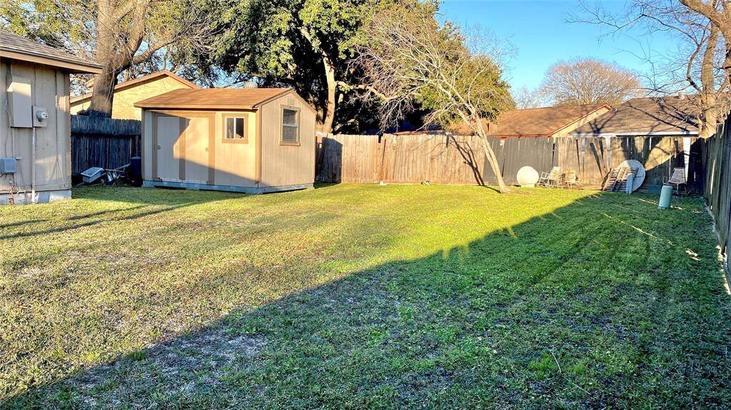 This spacious backyard features a well-maintained lawn, a wooden storage shed, and is enclosed by a wooden fence, providing privacy and a great space for outdoor activities. Mature trees add shade and character to the area.