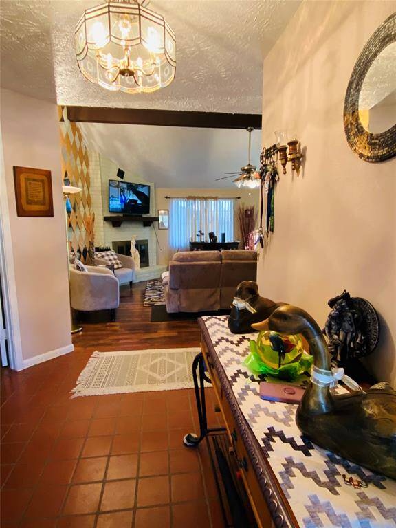 This inviting living space features warm, earthy tones with a cozy seating area, a fireplace, and a vaulted ceiling. The room is accented with decorative items and has a view through to a dining area. Natural light filters through curtains, creating a welcoming ambiance.