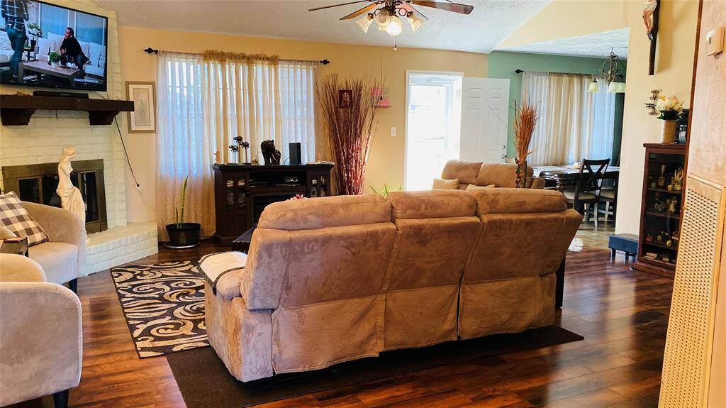 This cozy living area features warm wood flooring, a plush sectional sofa, and a fireplace. It opens to a dining space with ample natural light, offering a welcoming atmosphere for relaxation and entertaining.