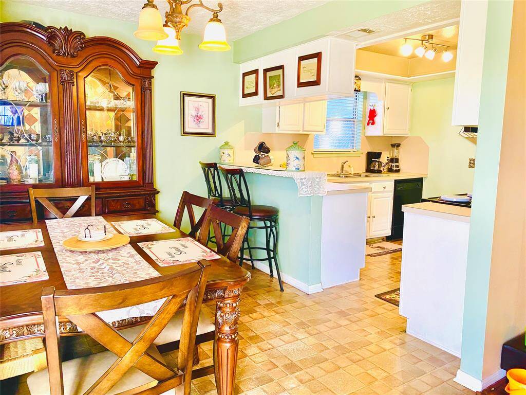 This inviting dining area features a classic wooden table set and an elegant china cabinet. It opens to a cozy kitchen with white cabinetry, a breakfast bar with seating, and ample natural light, creating a warm, welcoming atmosphere.
