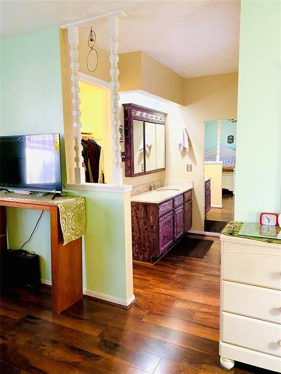 This photo shows a cozy bedroom area with hardwood floors, an attached vanity space featuring purple cabinetry, and a glimpse into a connected bathroom.