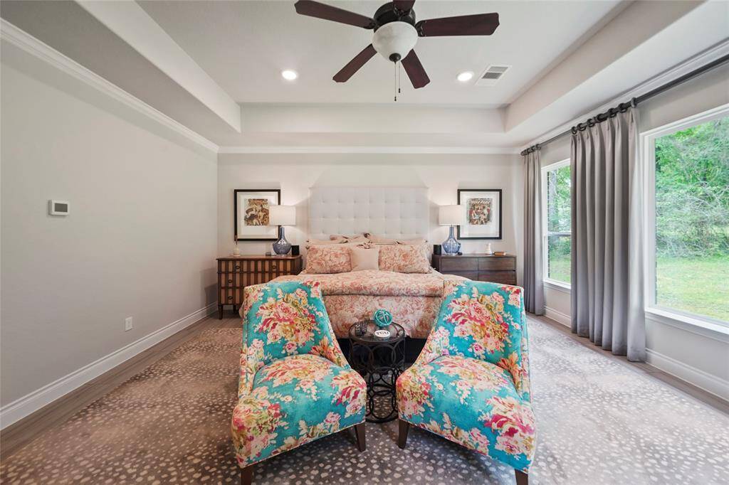 This primary bedroom makes for a private sanctuary and includes custom window coverings and tray ceiling.
