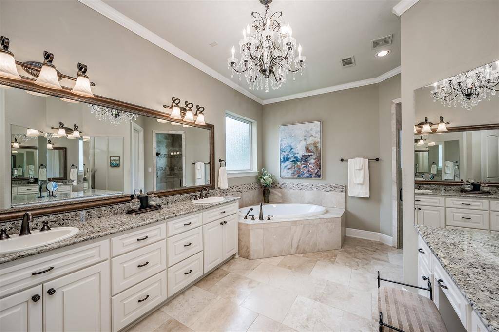 Indulge in a lavish spa bath that features a deep soaking Roman tub with handheld sprayer and a seated vanity/dressing area. The crystal chandelier adds opulence and can be dimmed for ambient lighting.