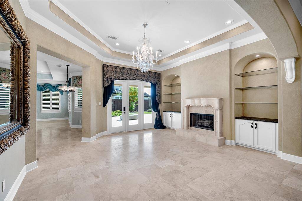 Adding symmetry to both sides of the stone fireplace are recessed arches with custom built cabinetry and artfully lit glass shelving. Glass panel doors open to a lushly landscaped backyard retreat.