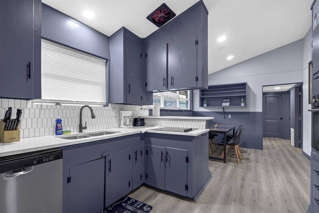 Discover a sleek kitchen featuring blue cabinets, white countertops, a hexagonal backsplash, and stainless steel appliances, seamlessly connected to a cozy dining area.