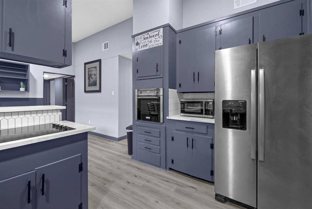 Elegant kitchen featuring blue cabinetry, stainless steel appliances, white countertops, and hardwood floors, all wrapped in a cozy, modern design.