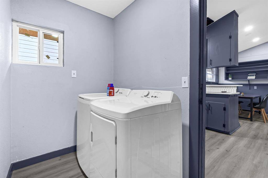 Discover a pristine laundry room featuring a top-loading washer, dryer, and stylish blue cabinets, all illuminated by natural light from a charming window.