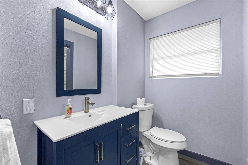 Discover a sleek bathroom featuring calming blue walls, a stylish navy vanity, a crisp white sink, a modern mirror, and a window offering natural light with privacy blinds.