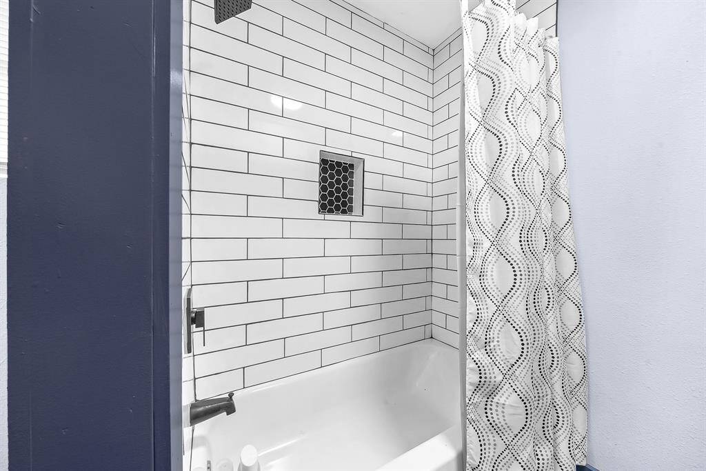 A sleek bathroom featuring elegant white subway tiles, striking dark accents, a cozy bathtub, and a stylish patterned shower curtain.
