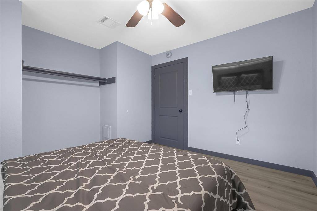 Explore this sleek bedroom featuring a stylish bedspread, wall-mounted TV, ceiling fan, and ample closet space.