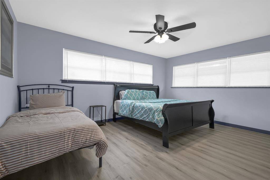 Inviting bedroom featuring two beds, elegant hardwood floors, calming blue walls, and abundant natural light with white blinds and a ceiling fan.