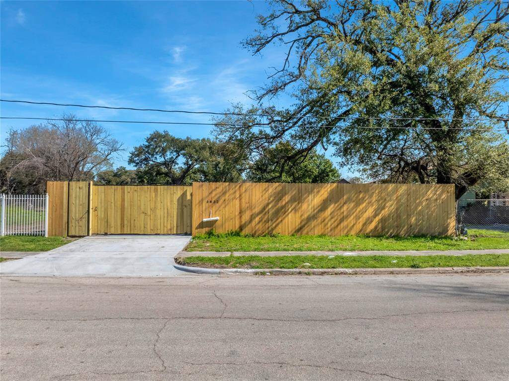 Vacant lot with a new wooden privacy fence and a concrete driveway entrance, a ready-to-build homesite in a neighborhood with mature trees.