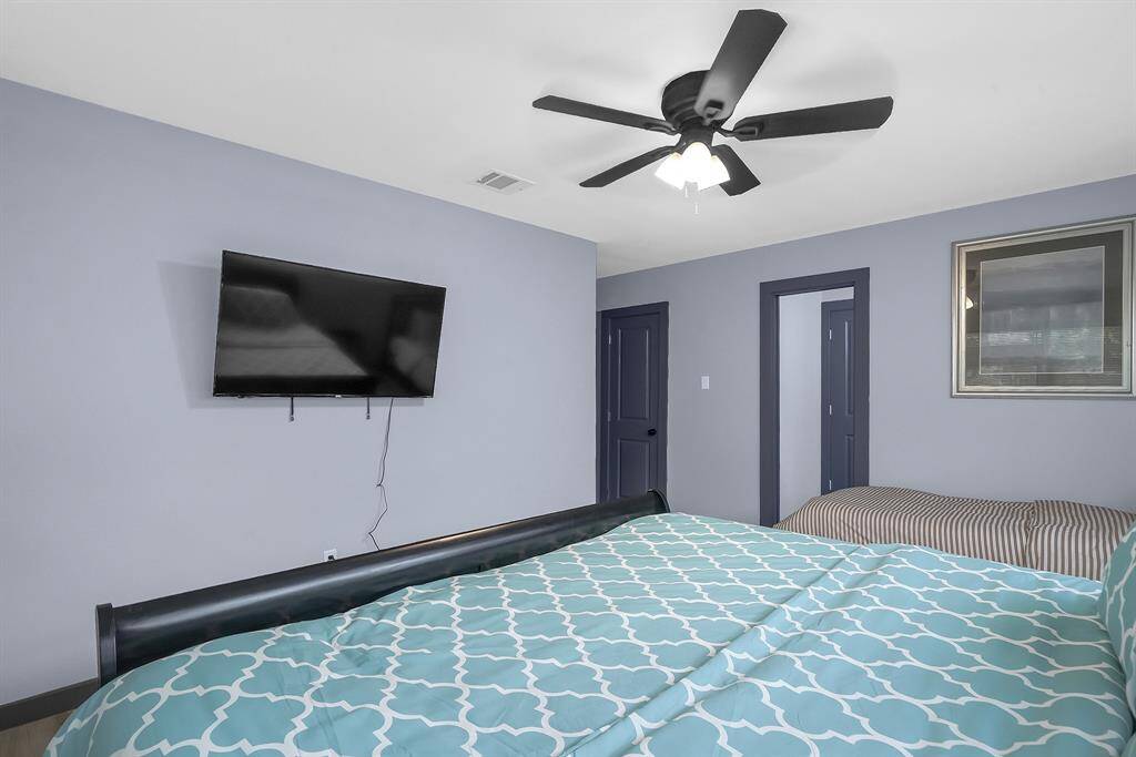 Inviting bedroom featuring a stylish bedspread, wall-mounted TV, ceiling fan, and convenient dual-door access.