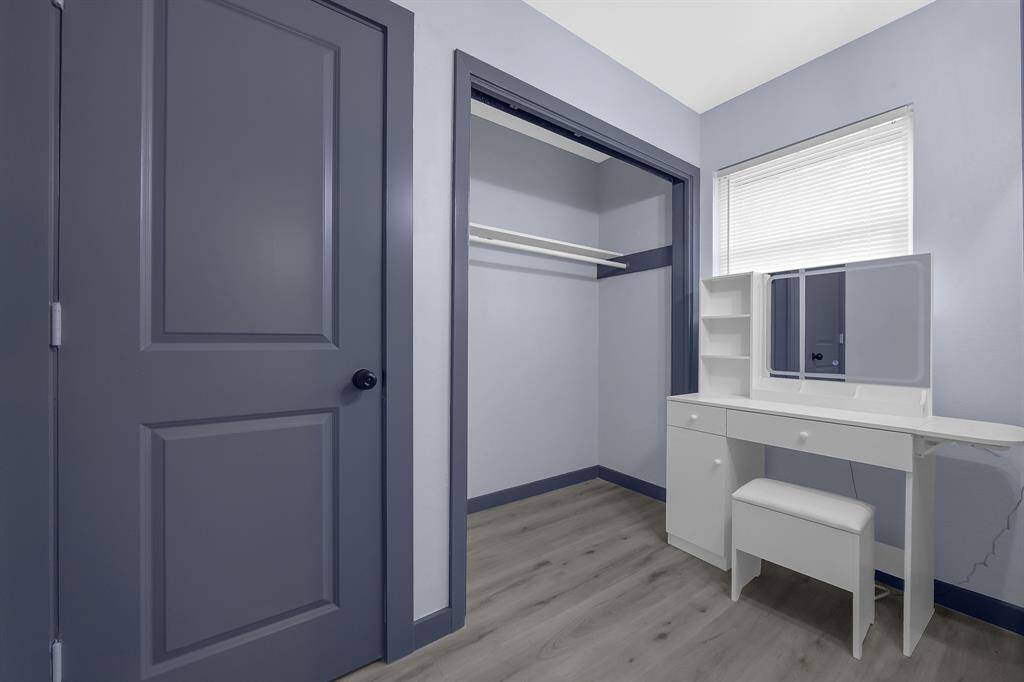 Discover a sleek blue and white room featuring a built-in closet, stylish desk, and ample shelving. Enjoy natural light through a window with blinds, perfect for a serene workspace or retreat.