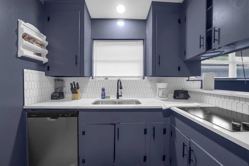 Chic kitchen featuring sleek blue cabinets, pristine white countertops, and premium stainless steel appliances, all enhanced by a bright window above the sink.