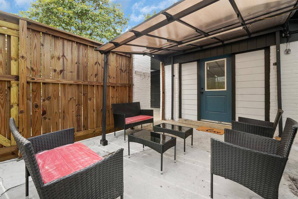 Charming outdoor patio featuring stylish wicker furniture with red cushions, a wooden fence for privacy, and a pergola with a translucent cover next to a white brick wall. Perfect for relaxation and entertaining.