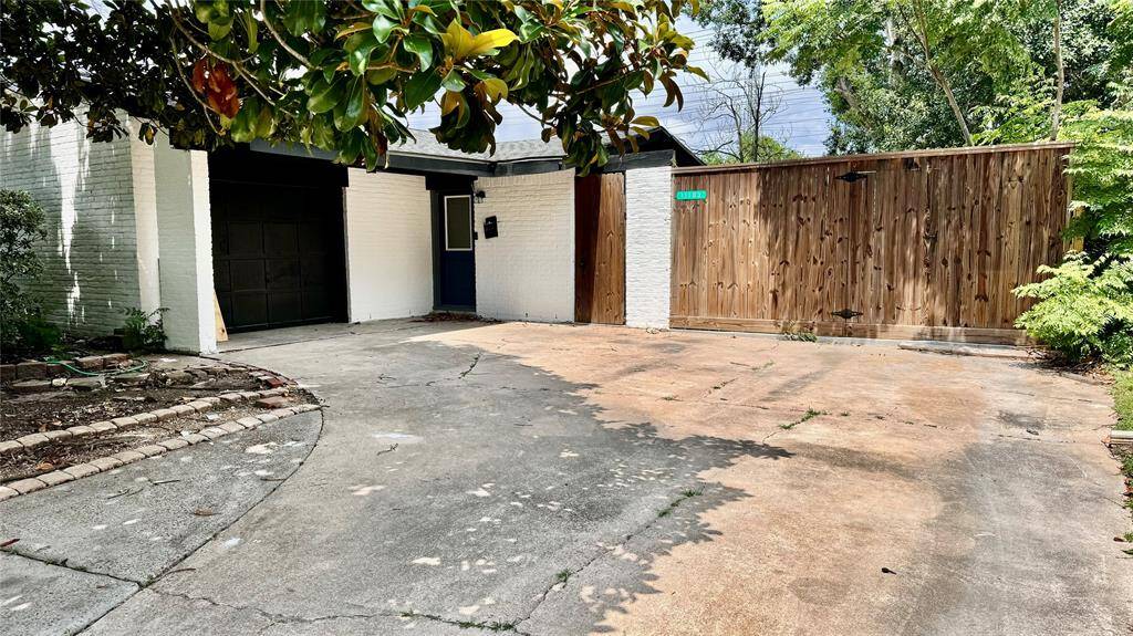 Expansive driveway leading to a white-walled garage, complemented by a charming wooden fence, all under a bright, sunny sky.