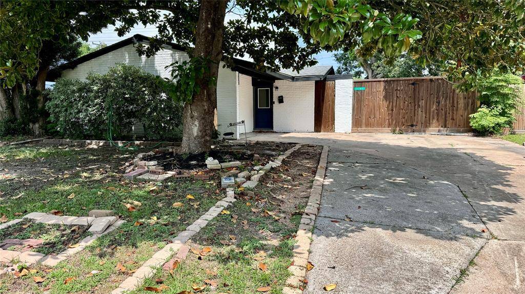 Charming suburban home featuring a spacious driveway, elegant wooden gate, and a lush garden shaded by mature trees. Perfect for those seeking a serene retreat with plenty of potential.
