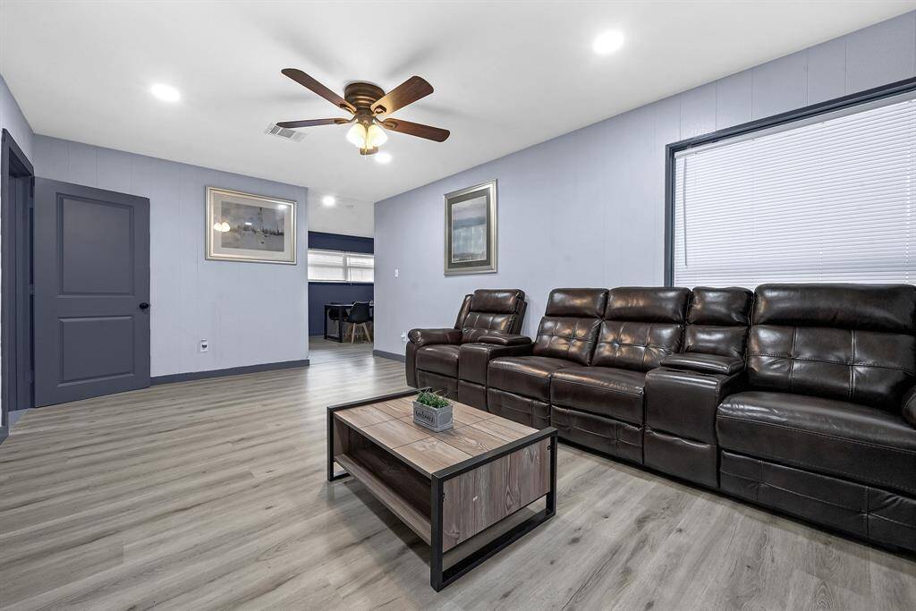 Experience modern elegance in this living room, featuring a spacious brown leather couch, sleek coffee table, ceiling fan, and stylish hardwood floors in a soothing neutral palette.