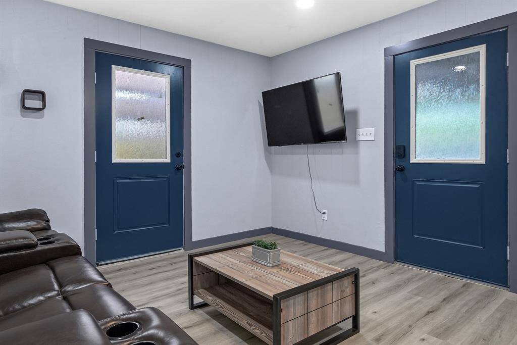 Experience modern living in this stylish room featuring sleek gray walls, vibrant blue doors, a wall-mounted TV, a plush dark sofa, and a chic wooden coffee table.