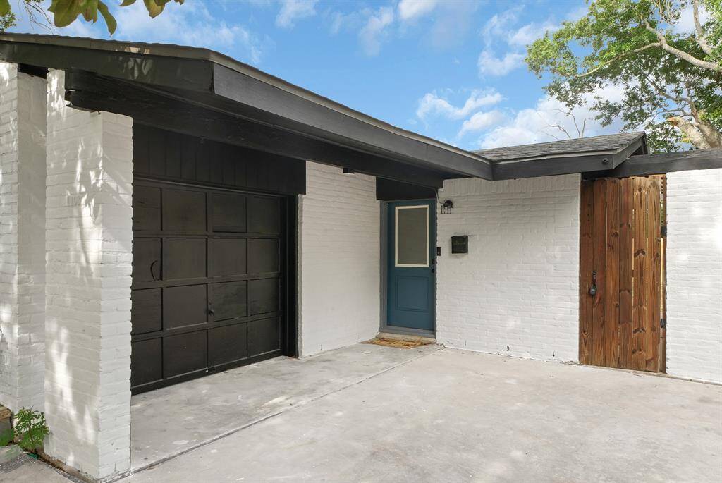 Charming white brick home with a striking black garage, inviting blue front door, and a rustic wooden gate, all set against a clear sky.