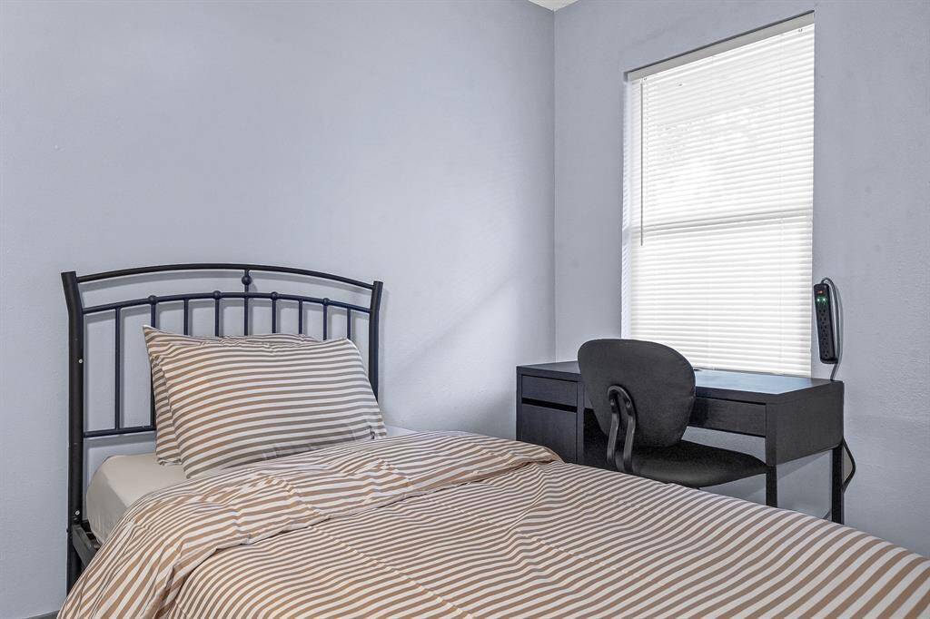 Cozy bedroom featuring a stylish metal bed frame with a striped bedspread, complemented by a functional desk and chair. The window with blinds offers privacy and natural light.