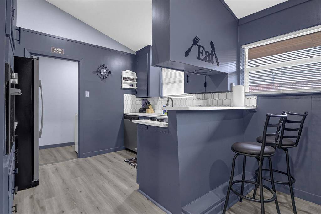 Sleek kitchen featuring vibrant blue walls, chic bar stools, and stainless steel appliances, with a charming "Eat" sign adding a delightful touch above the sink.