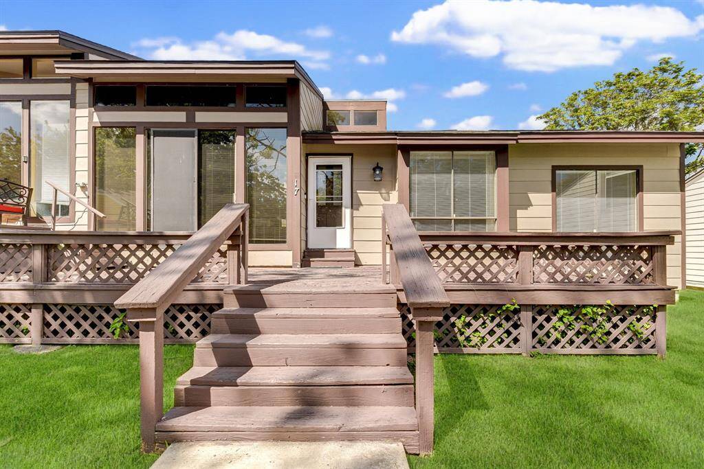 This photo showcases a charming home with a welcoming front porch, featuring a wooden staircase and railing. The exterior is accented with large windows, allowing ample natural light, and is surrounded by a well-maintained lawn.