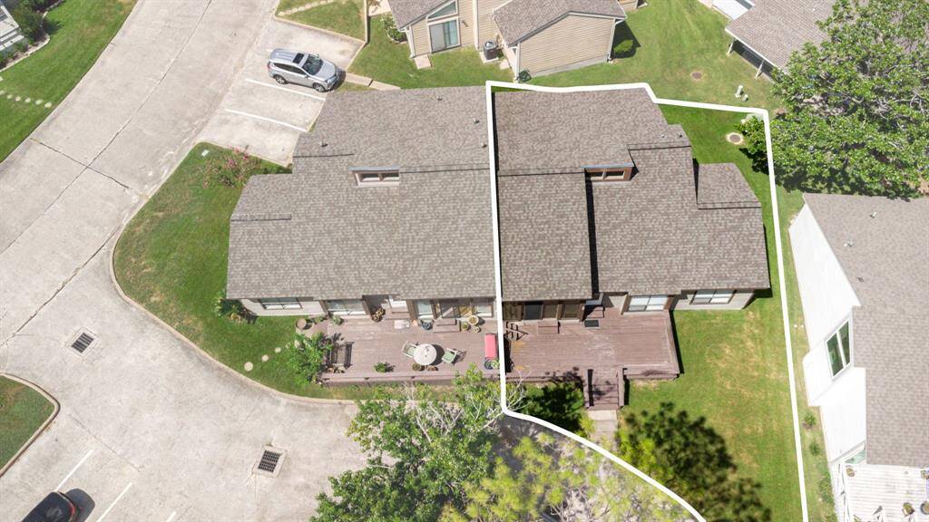 This aerial photo showcases a spacious, home with a large deck, ample yard space, and adjacent parking.