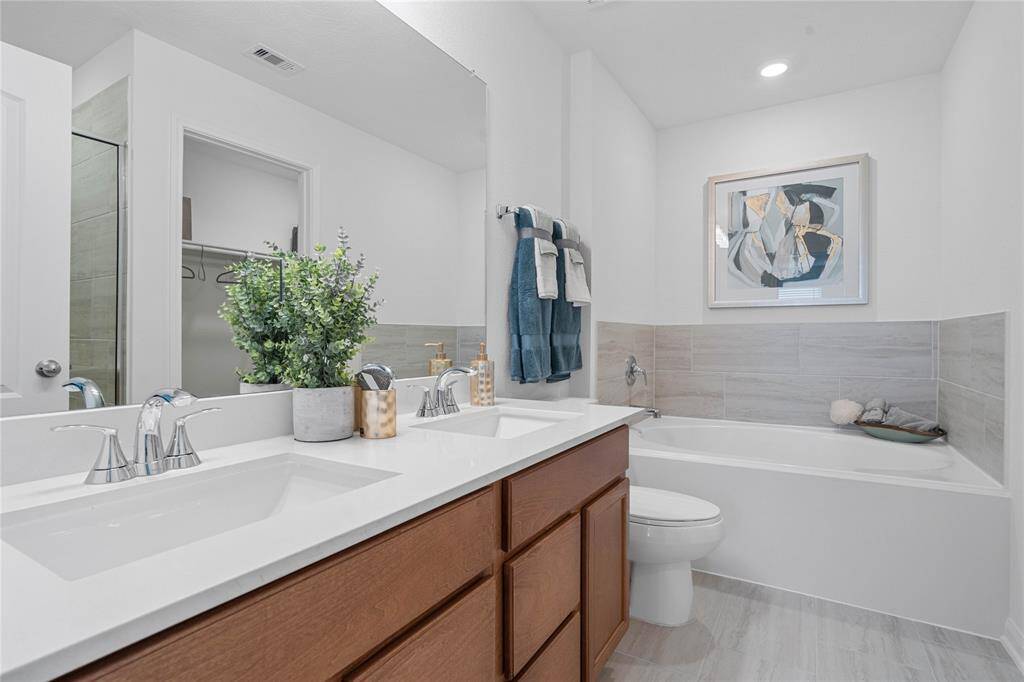 This primary bathroom is definitely move-in ready! Featuring stained cabinets with light countertops and dual vanities, oversized garden tub with custom tile, high ceilings, custom paint, sleek and dark modern finishes.