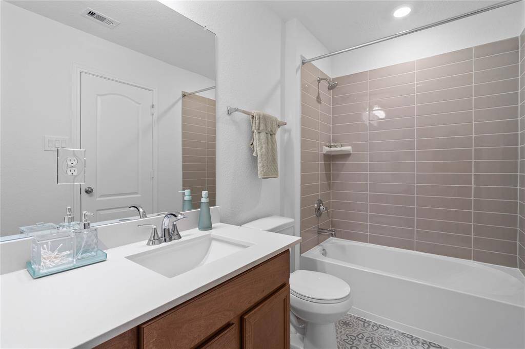 Secondary bath features tile flooring, stained wood cabinet, beautiful light countertops, mirror, dark, sleek fixtures and modern finishes.
