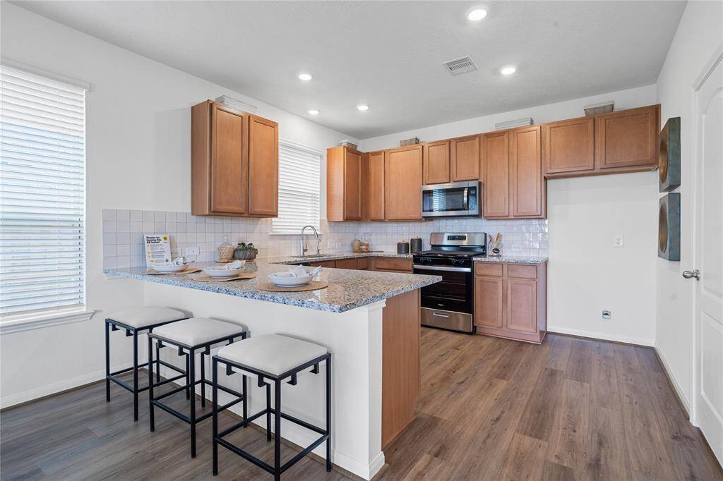 This spacious kitchen features high ceilings, Woodmont Cody flat panel cabinets, granite countertops, SS appliances, modern tile backsplash, recessed lighting, extended counter for breakfast bar, and a pantry all overlooking your huge family room.