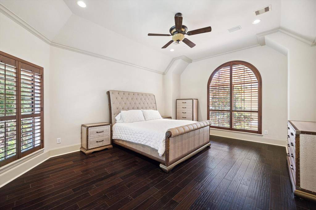 The tranquil primary suite boasts beautiful hardwood flooring, crown molding, recessed lighting, a ceiling fan with light, expansive windows, and a door that opens onto the private balcony.