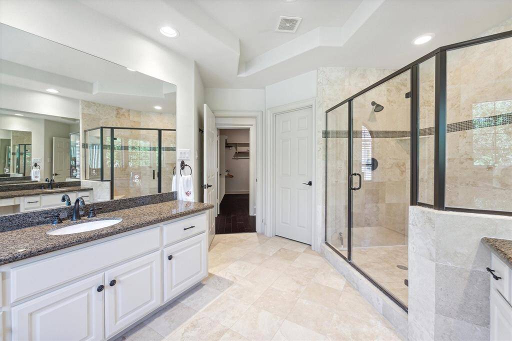 The primary bath features an expansive glass shower with dual shower heads and tile that extends all the way to the ceiling.