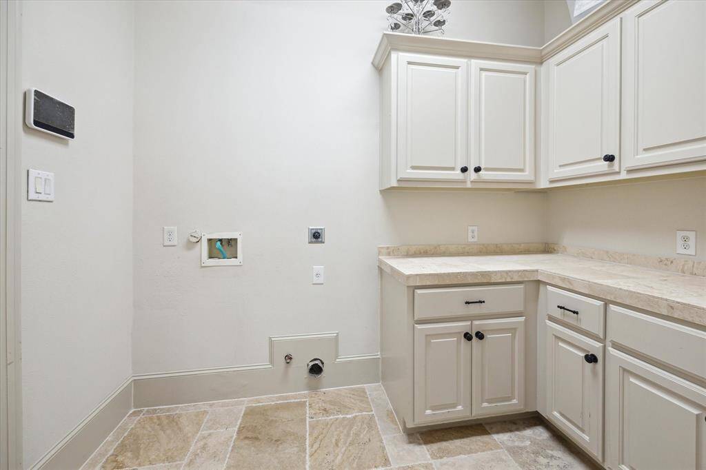 Adjacent to the kitchen and garage, the utility room boasts travertine flooring, built-in cabinets and a stone countertop.