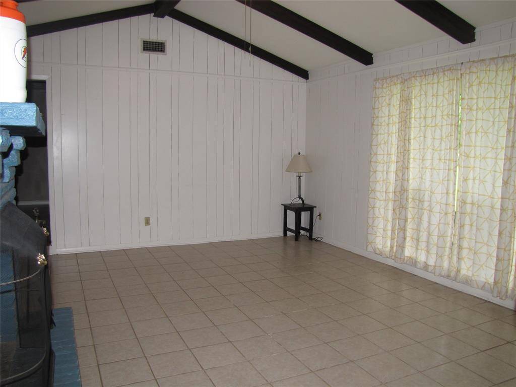 Spacious, versatile room with tiled flooring, white paneled walls, and exposed beams, suitable for a family room, game room, or dining area.