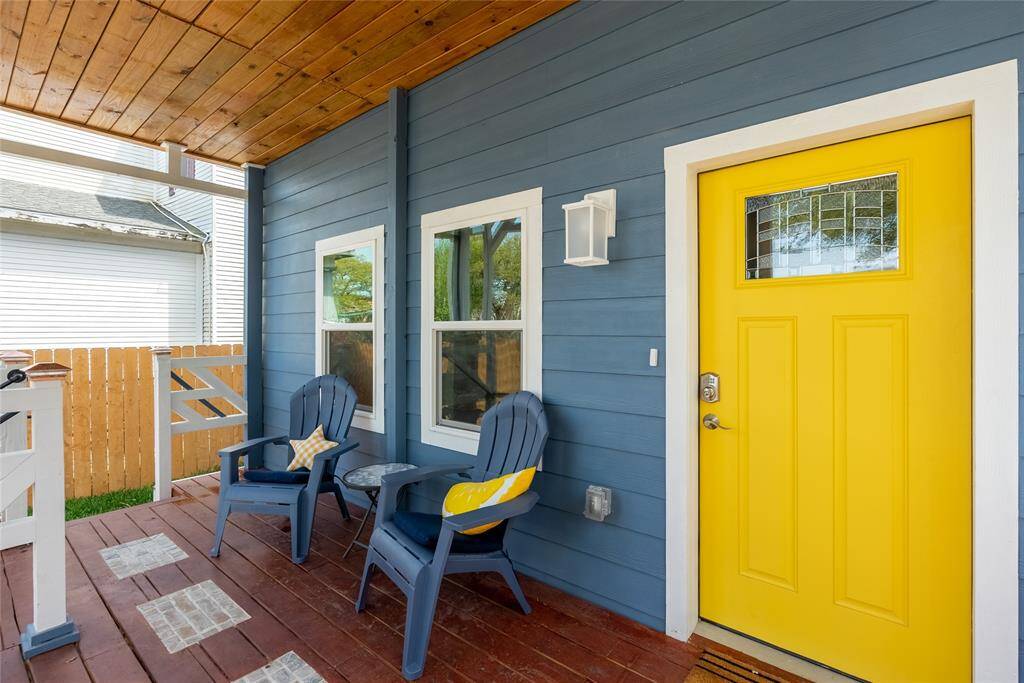 This is a cozy, covered front porch with a cheerful yellow door and a pair of comfortable Adirondack chairs for relaxing. It features a wooden ceiling that adds warmth to the space and a well-maintained blue siding exterior.