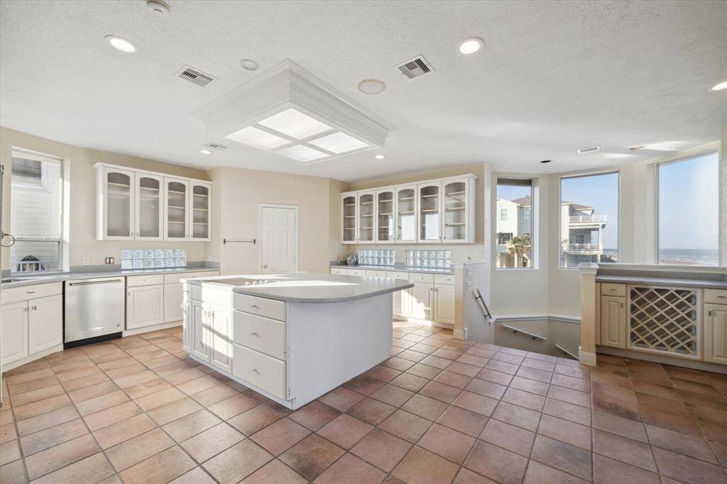 Bright, spacious kitchen with white cabinetry, tile floor, skylight, and ocean views through large windows.