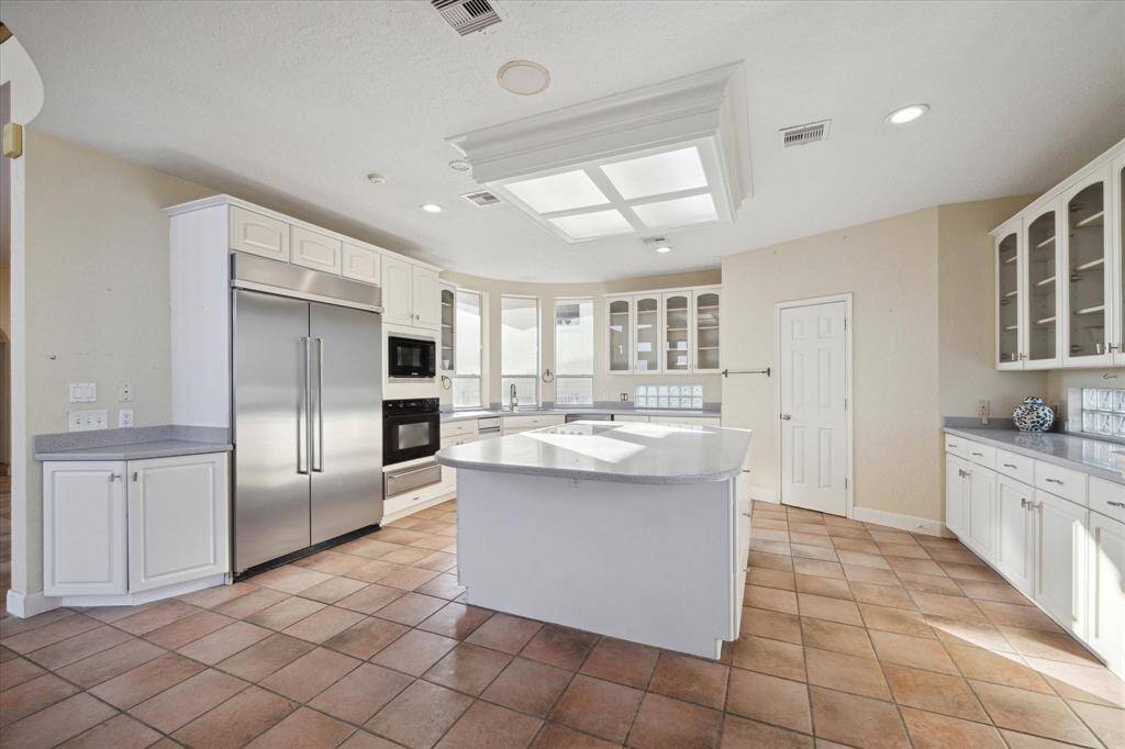 Bright, spacious kitchen with white cabinets, stainless steel appliances, tile flooring, and skylight.