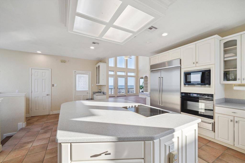 Bright, spacious kitchen with white cabinetry, stainless steel appliances, tile flooring, and a view of the outside through large windows.