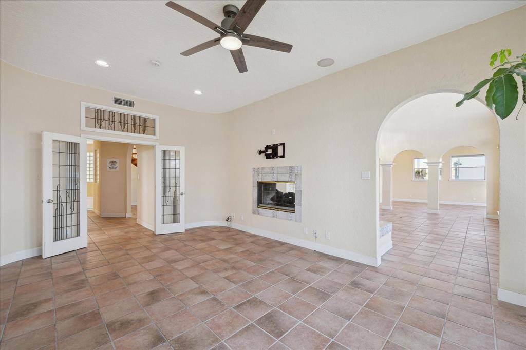 Spacious, either 5th bedroom or second den that is 20 ft by 12 ft, arched doorways, a fireplace, ceiling fan, and French doors leading to another room.