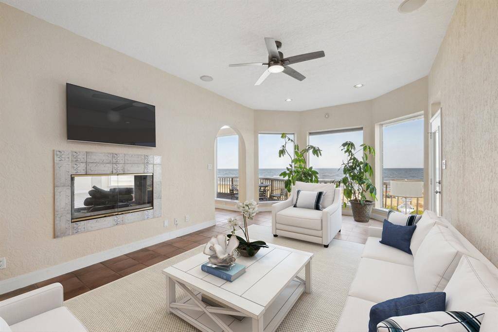 Bright, contemporary living room with ocean view, modern furniture, fireplace, mounted TV, and ceiling fan. This room has been virtually staged (20ft by 12ft)