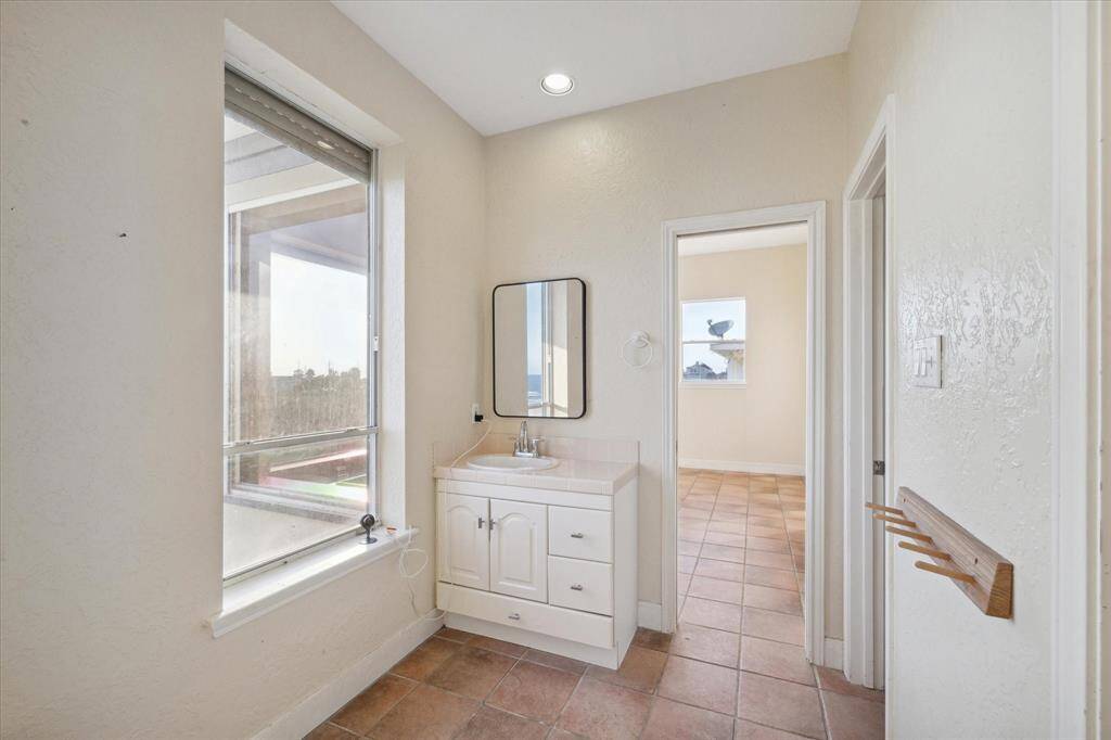 A bathroom with a vanity cabinet, mirror, window, and a view into an adjoining room with ocean views.