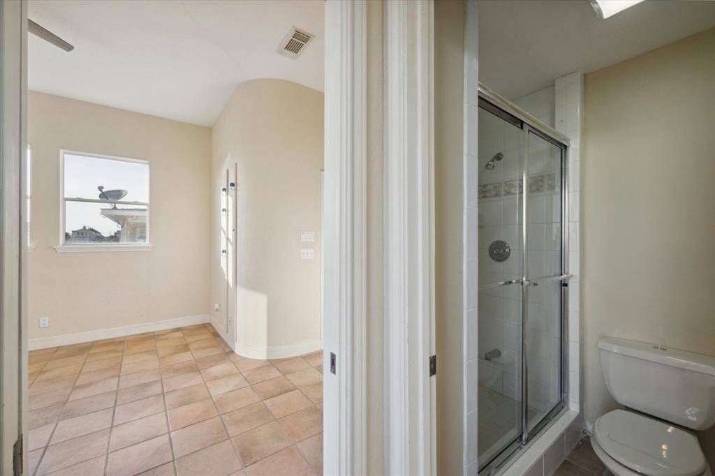 A bathroom with a shower stall, toilet, tiled floor, and a window with an exterior breathtaking ocean view.