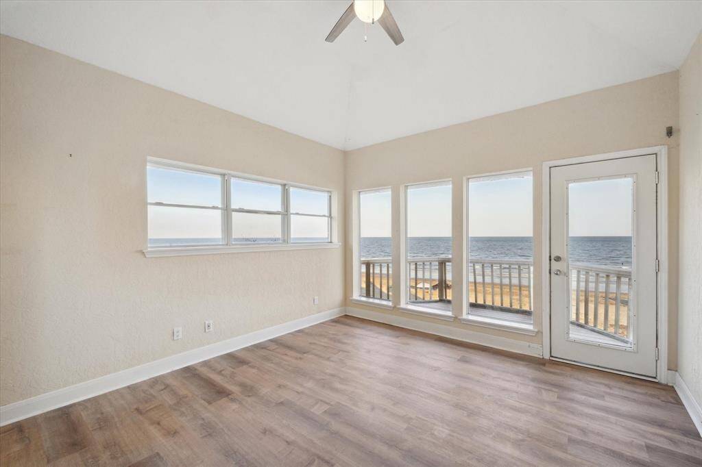 One of the primary  beachfront bedrooms room with large windows, a glass door, wooden flooring, and a view of the ocean and sky.